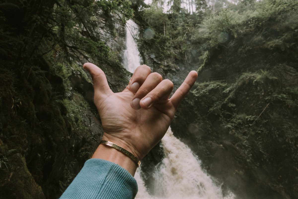 Homme faisant le signe du shaka devant une cascade dans une forêt 