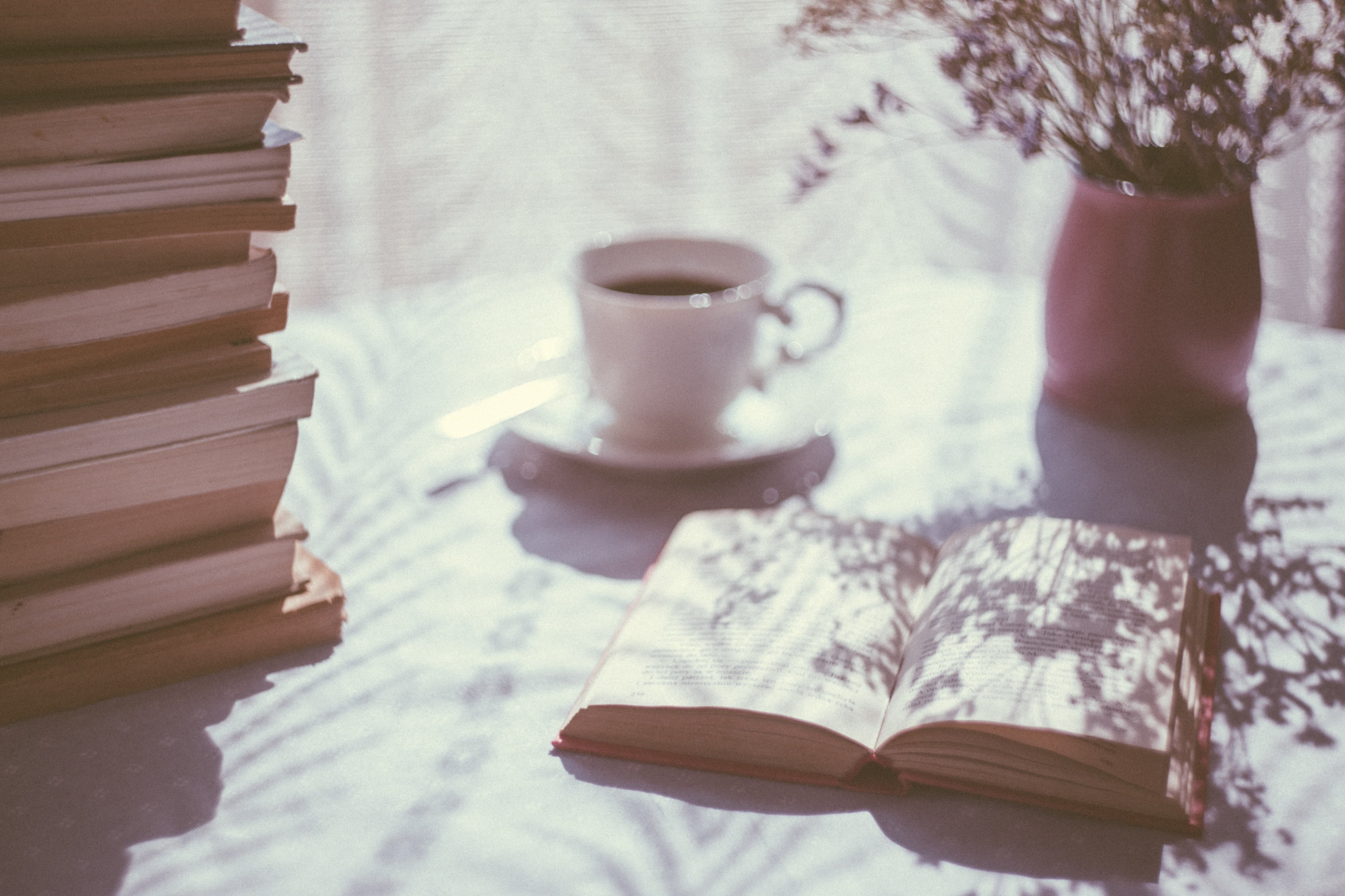 Table ensoleillée avec une pile de livres citations prendre le temps, une tasse de café et un vase fleuri